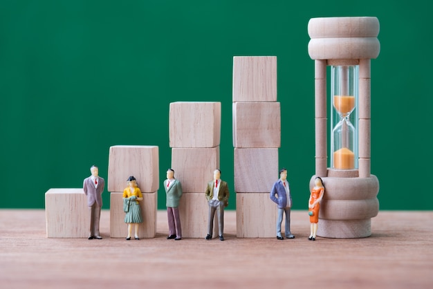 Photo stack of wood cube building blocks and miniature people on wooden table and green background