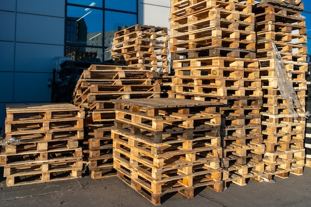 A stack of wooden pallets in an internal warehouse an outdoor\
pallet storage area under the roof next to the store piles of\
eurotype cargo pallets at a waste recycling facility