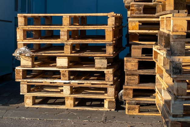 A stack of wooden pallets in an internal warehouse an outdoor\
pallet storage area under the roof next to the store piles of\
eurotype cargo pallets at a waste recycling facility