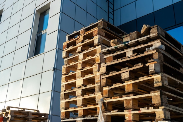 A stack of wooden pallets in an internal warehouse an outdoor\
pallet storage area under the roof next to the store piles of\
eurotype cargo pallets at a waste recycling facility