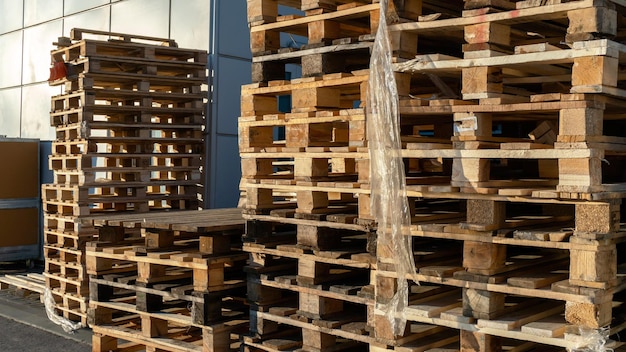 A stack of wooden pallets in an internal warehouse An outdoor pallet storage area under the roof next to the store Piles of Eurotype cargo pallets at a waste recycling facility