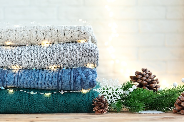 Stack of wool knitted clothes on wooden table  with festive bokeh.