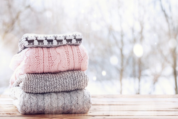 Stack of wool knitted clothes on wooden tableon winter background