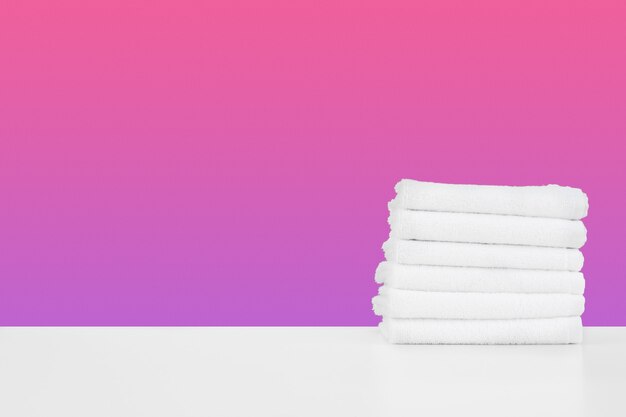 Stacked clean towels on white table against color background