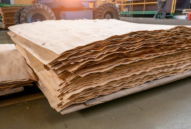 Stacked plywood and wooden board products against defocused blurred piece of industrial warehouse storage on production site Copy space Selective focus