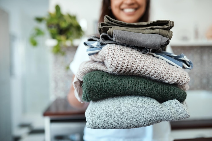 Photo stacked and ready to be packed closeup shot of a young woman holding a pile of folded laundry at home