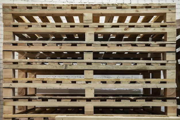 Photo stacked used wooden pallets in warehouse. stacks of euro-type cargo pallets. background of wooden pallets. concept of warehousing and storage of goods