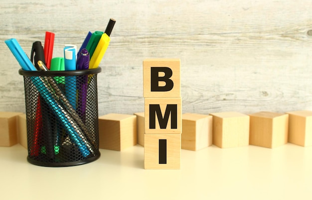 Stacked wooden cubes with letters BMI on a white work table on a textured gray background