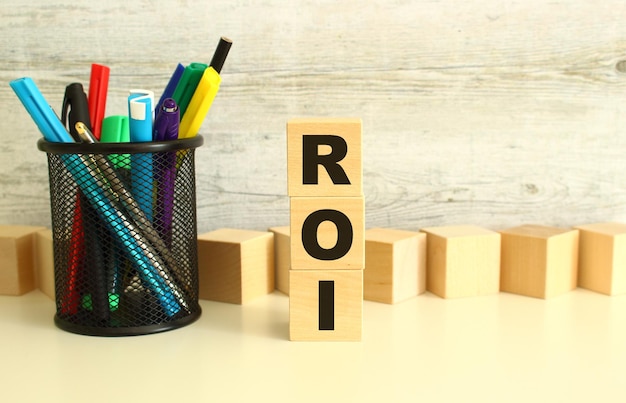 Stacked wooden cubes with letters ROI on a white work table on a textured gray background