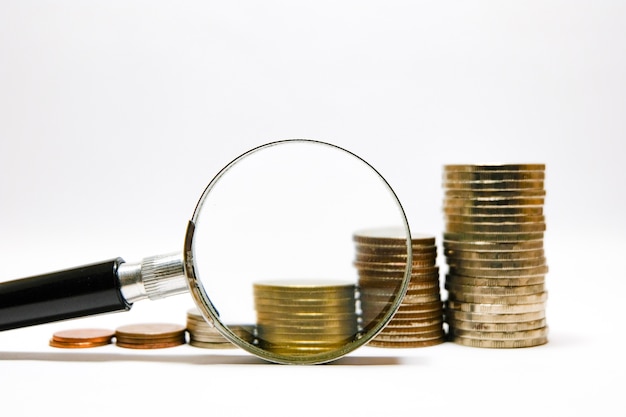 Stacking coins money growing and increasing with magnifier glass on white background.