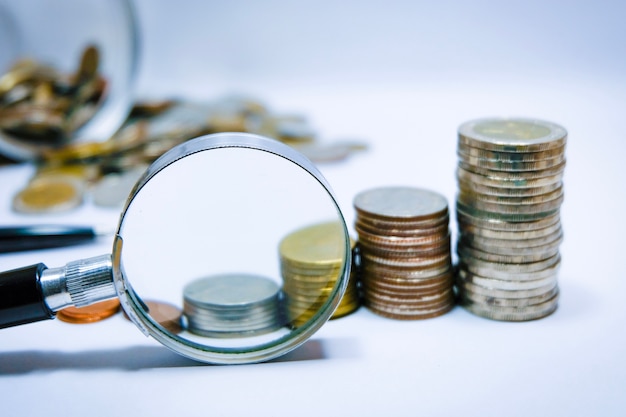 Magnifying glass and coins on the white desk.