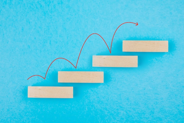 Photo stacking of wooden blocks in the form of a step ladder with a red up arrow on a blue background a ladder of success in the concept of business growth copy space