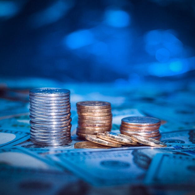 Stacks of coins on the background of one hundred dollar bills. Dark blue light.