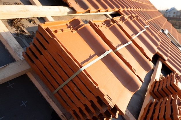 Stacks of yellow ceramic roofing tiles for covering residential building roof under construction.