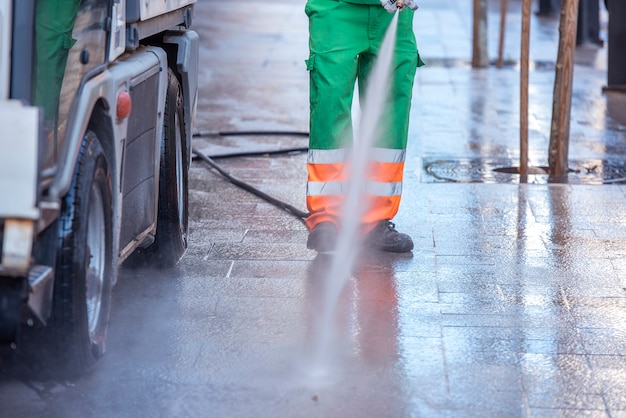 Stadsarbeider met een waterdrukpistool. Reiniging van straten en straatmeubilair, ter voorkoming van covid19, coronavirus