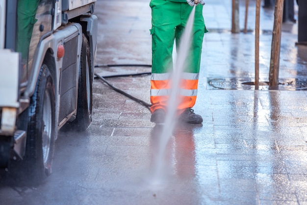 Stadsarbeider met een waterdrukpistool. Reiniging van straten en straatmeubilair, ter voorkoming van covid19, coronavirus