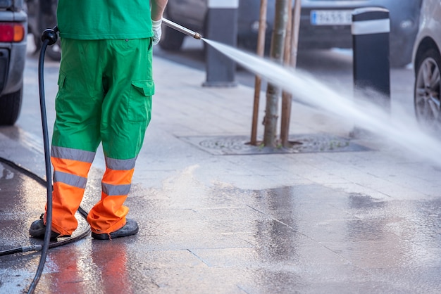 Stadsarbeider met een waterdrukpistool. Reiniging van straten en straatmeubilair tijdens epidemie