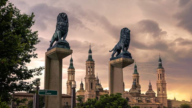 Stadsgezicht weergave van bronzen leeuwen sculptuur op de brug met de daken en torenspitsen van de basiliek van onze lieve vrouw achtergrond in de stad Zaragoza. Oriëntatiepunt monument Kathedraal van Aragon. Katholieke kerk Spanje