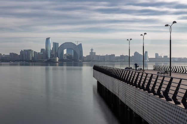 Stadshorizon weerspiegeld in water en lege pier met eenzame visser op de voorgrond Baku Azerbeidzjan