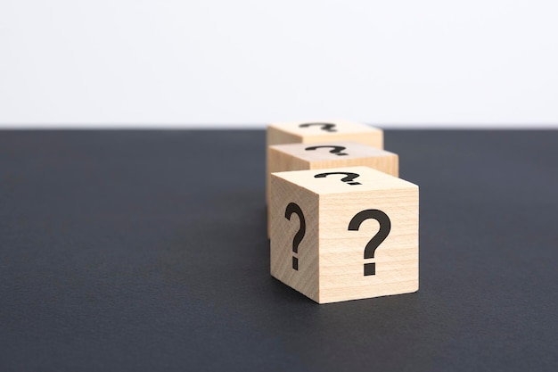 Staggered row of three wooden blocks with question marks black on black table copy space