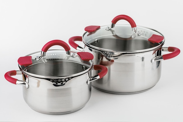 Stainless casserole with glass lid and red handles on grey background Kitchen concept