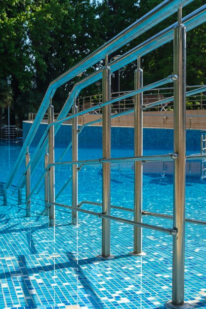 Stainless ladder and handrails in outdoors swimming pool on\
summer sunny day seaside vacation and hotel resort concept entrance\
in blue clean sea water pool