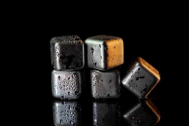 Stainless steel cubes simulating ice for cooling drinks on a black surface with a reflection