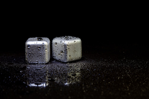 Stainless steel cubes simulating ice for cooling drinks on a black surface with a reflection.