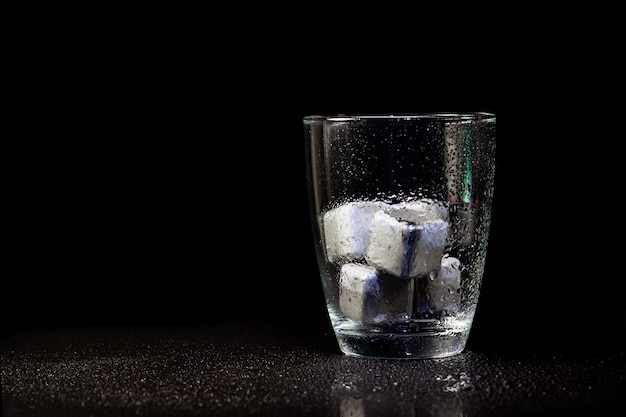 Stainless steel cubes simulating ice in whisky glass on a black table.