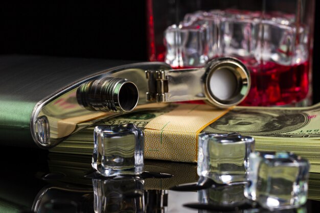 Stainless steel flask liquor alcohol and ice on table with glass on dollar banknote