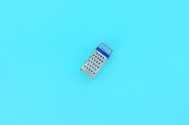 Photo stainless steel grater lies on a pastel colored paper. kitchen accessories. tools for cooking. flat lay top view