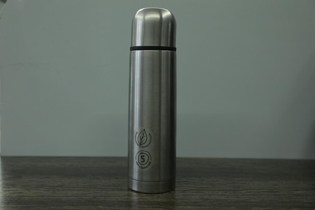 Stainless steel thermos on wooden table with grey background