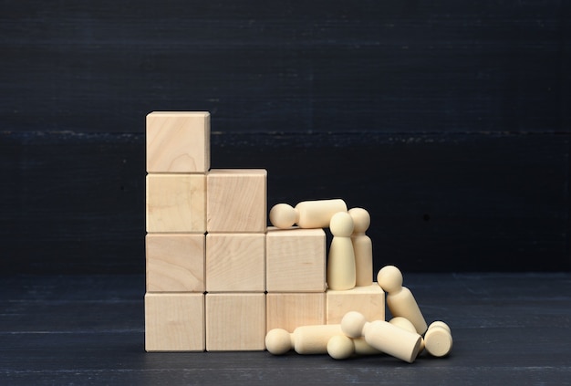 Stairs from wooden cubes and a crowd of fallen wooden figures\
of men on a blue surface