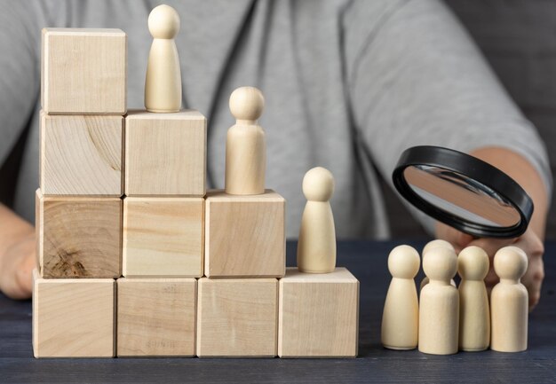 Foto scale fatte di cubi di legno e statuette di uomini una mano con una lente d'ingrandimento esamina il gruppo