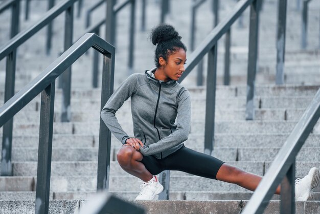 On the stairs Young african american woman in sportive clothes have workout outdoors at daytime