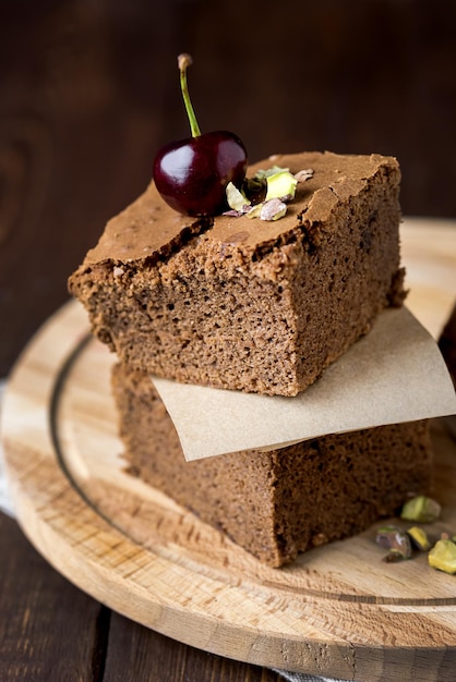 Stak van smakelijke zelfgemaakte chocolade brownies versierd met kersen en pistachenoten op houten dienblad