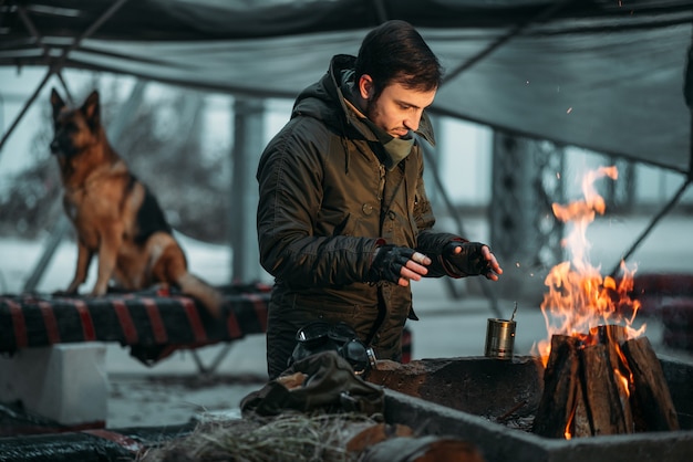 Stalker warms his hands on fire, dog. Post apocalyptic lifestyle on ruins, doomsday, judgment day