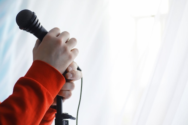Встаньте с микрофоном. Мужчина держит за руки микрофон на штативе. Выступление художника с микрофоном. Сцена с микрофоном.