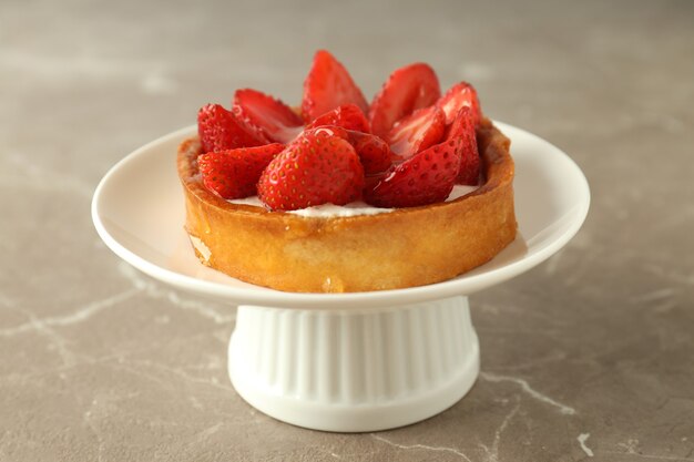 Stand with strawberry tart on gray textured table.