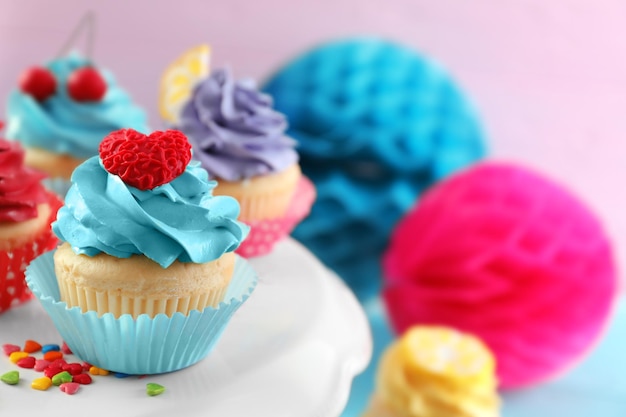 Stand with tasty bright cupcakes on blurred background closeup