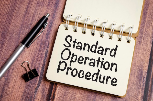 Standard operating procedure text on the paper notebook and pen\
on wooden background