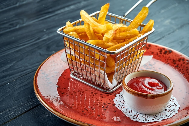 The standard side dish is French fries, served in a basket in a plate with red sauce. Black wood surface. Fast food