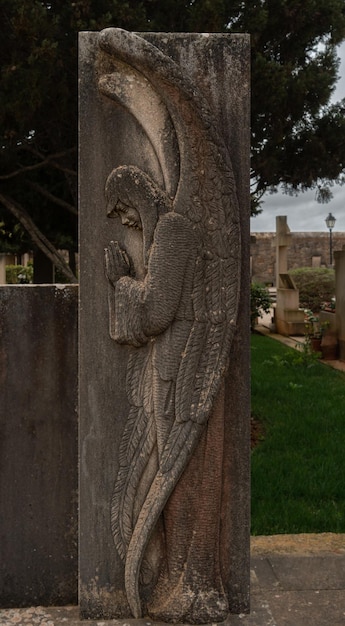 Standbeeld van een engel met vleugels biddend op een begraafplaats