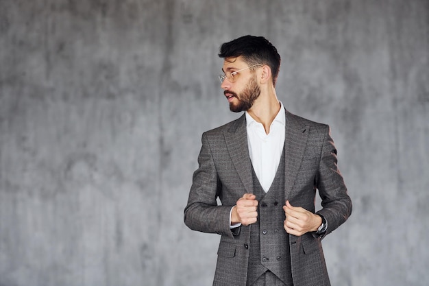 Standing against grey background Young stylish businessman in suit indoors Conception of success