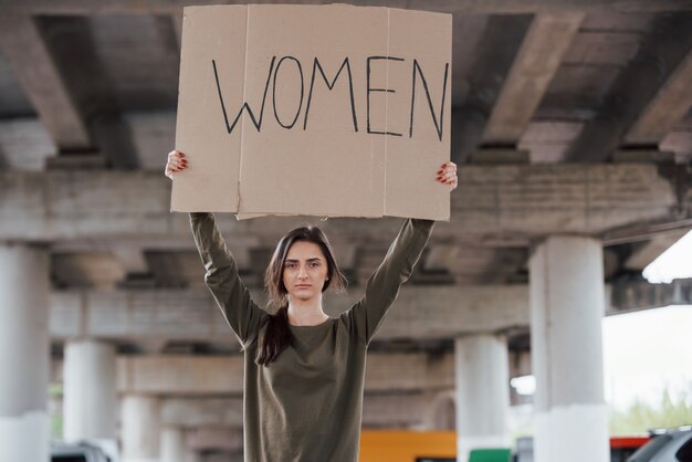 Standing alone. Pretty woman in casual clothes with handmade feminist poster in hands