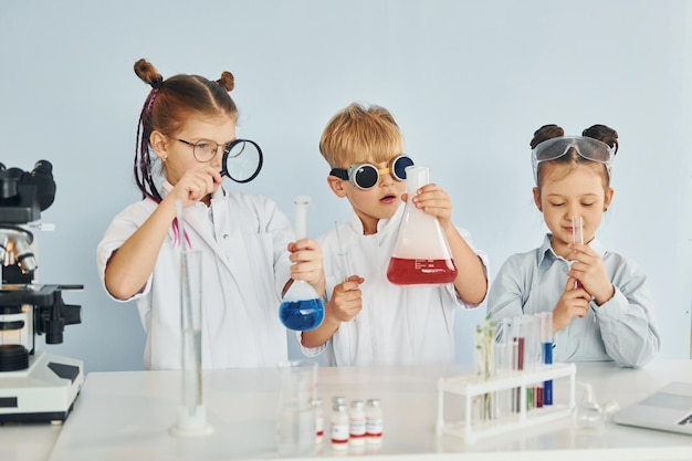 Foto in piedi accanto al tavolo con le provette bambini in camice bianco interpreta uno scienziato in laboratorio utilizzando attrezzature