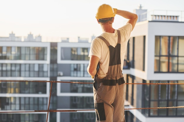 昼間建設で制服を着て働く若い男が高く立っている