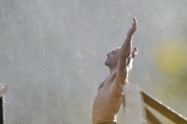 стоящий мужчина с широко раскрытыми руками на фоне водопадов, представляющий свежесть, здоровый образ жизни и концепцию успеха