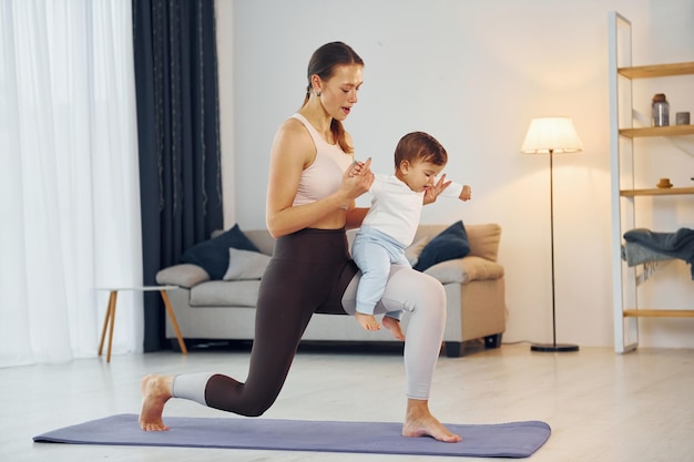 Standing on the mat and doing exerises mother with her little\
daughter is at home together