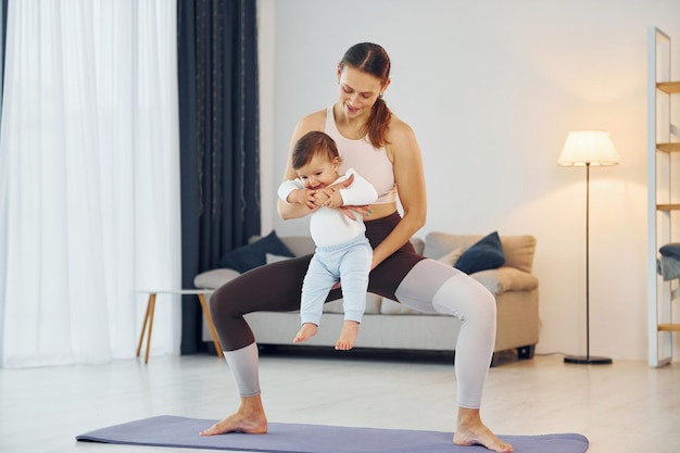 Standing on the mat and doing exerises Mother with her little daughter is at home together